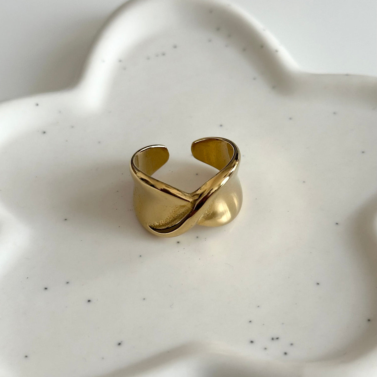 Bague Charlie dorée au design croisé et bombé présentée sur fond en céramique blanche.