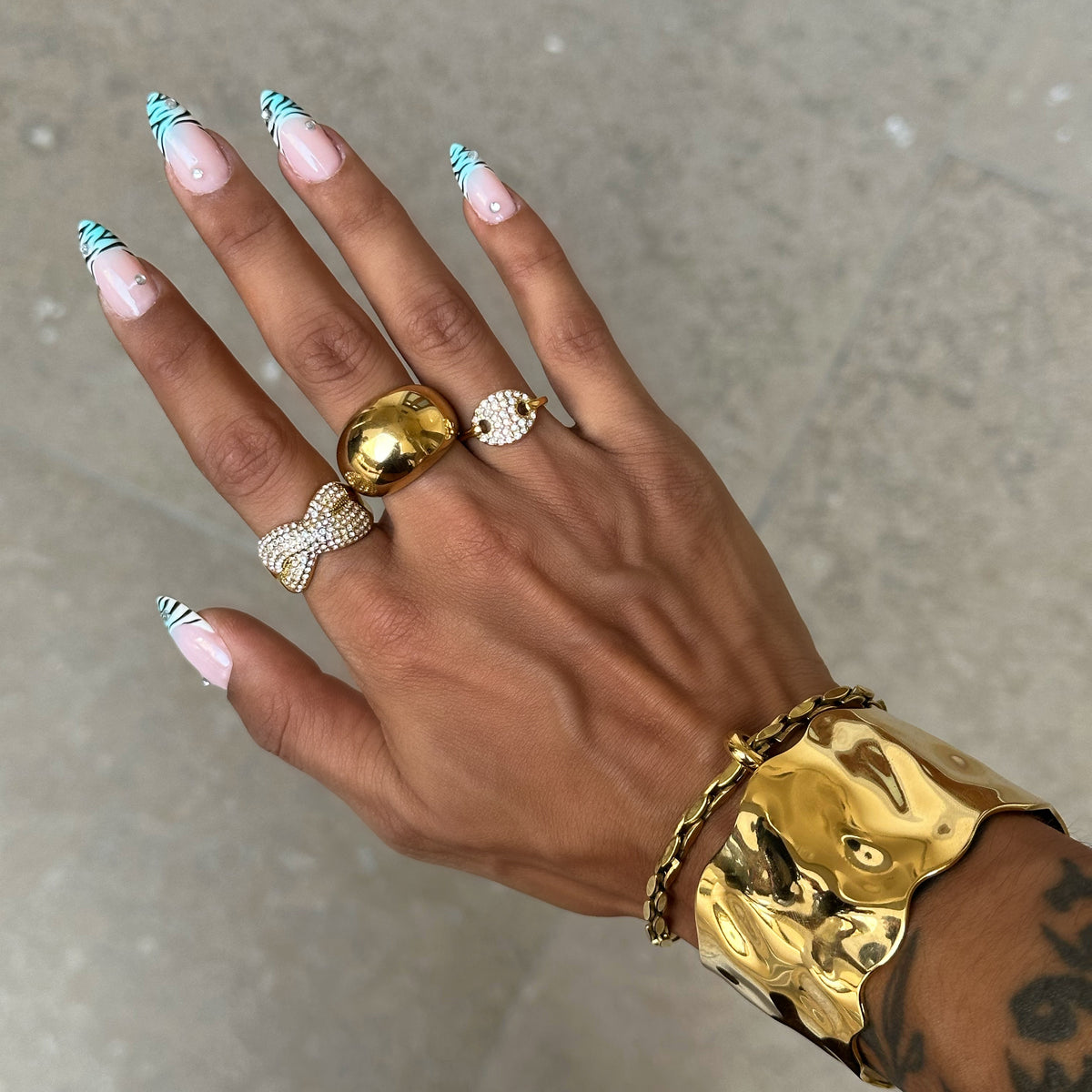 Bague Sasha dorée à strass portée avec une accumulation de bagues dorées