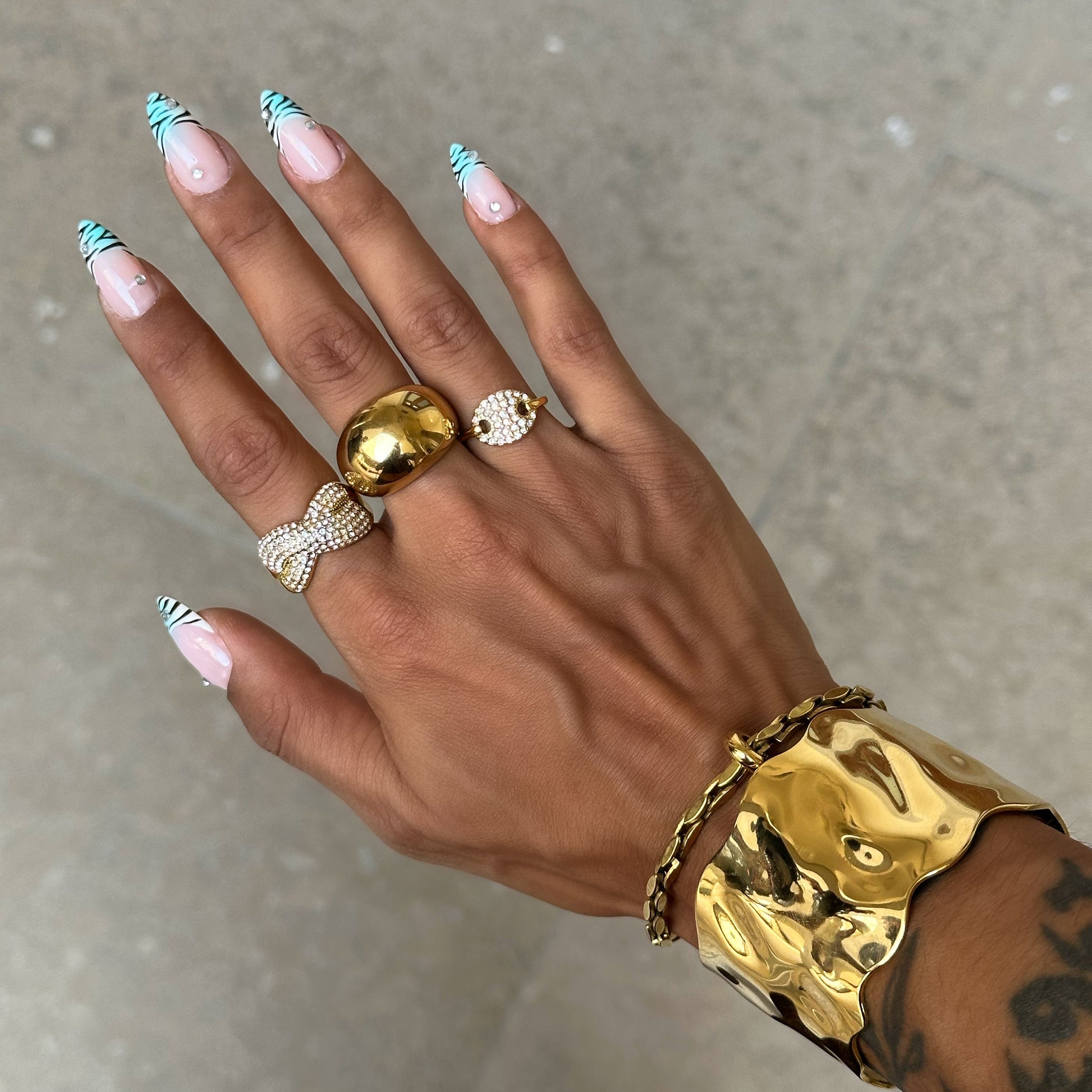 Bague Sasha dorée à strass portée avec une accumulation de bagues dorées