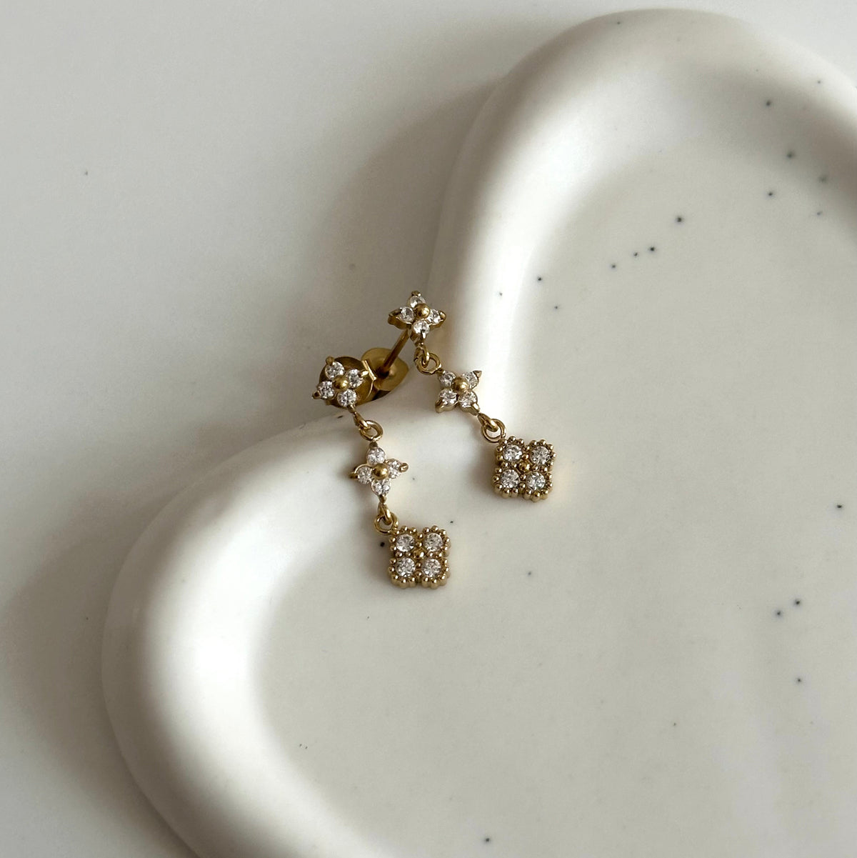 Boucles d’oreilles Line dorées pendantes ornées de zircons, présentées sur fond en céramique blanche.