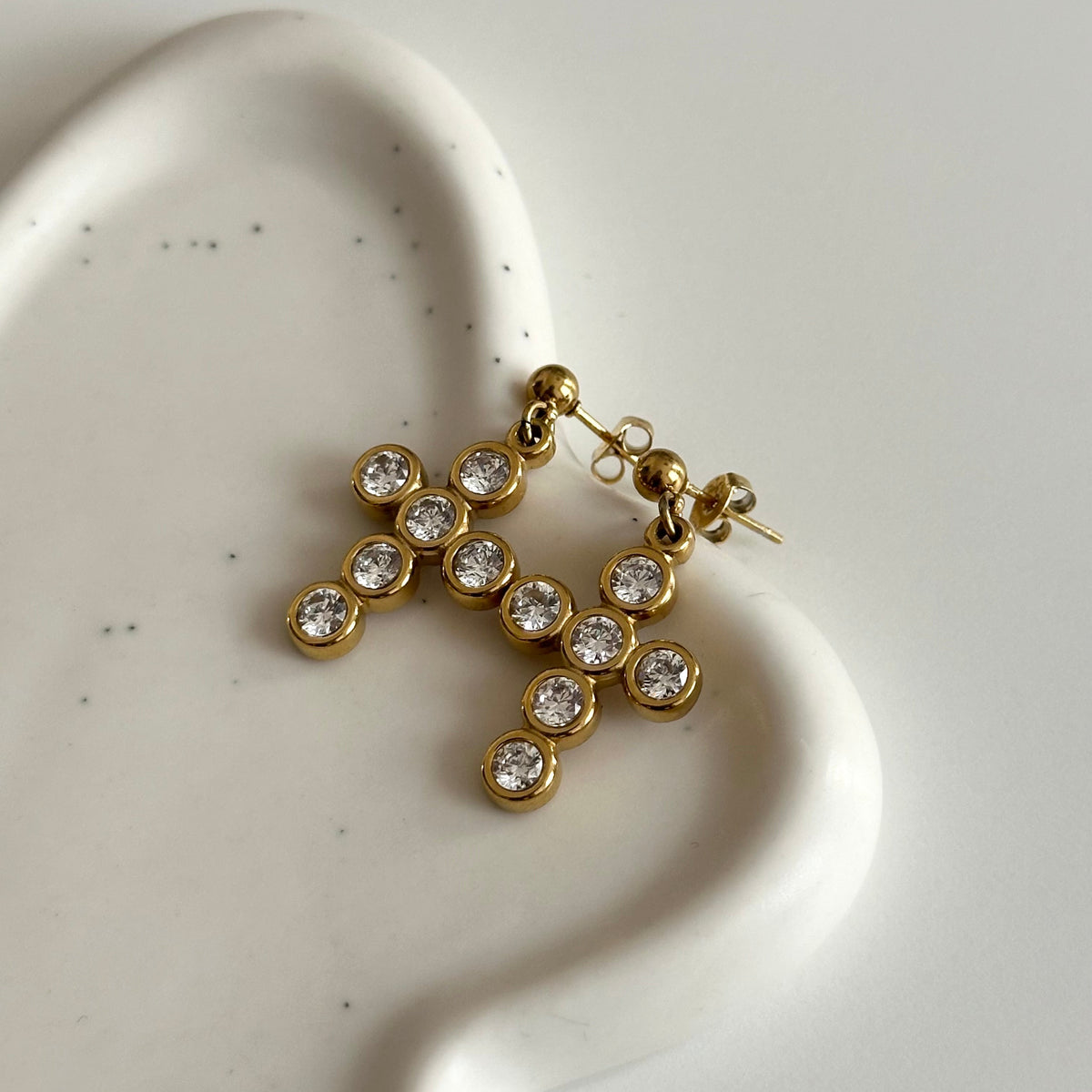 Vue rapprochée des boucles d’oreilles Livia en acier inoxydable PVD or 18K, avec croix dorées ornées de zircons.