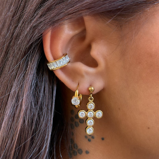 Boucles d’oreilles Livia en acier inoxydable PVD or 18K, pendentifs croix dorés ornés de zircons sur fond blanc.