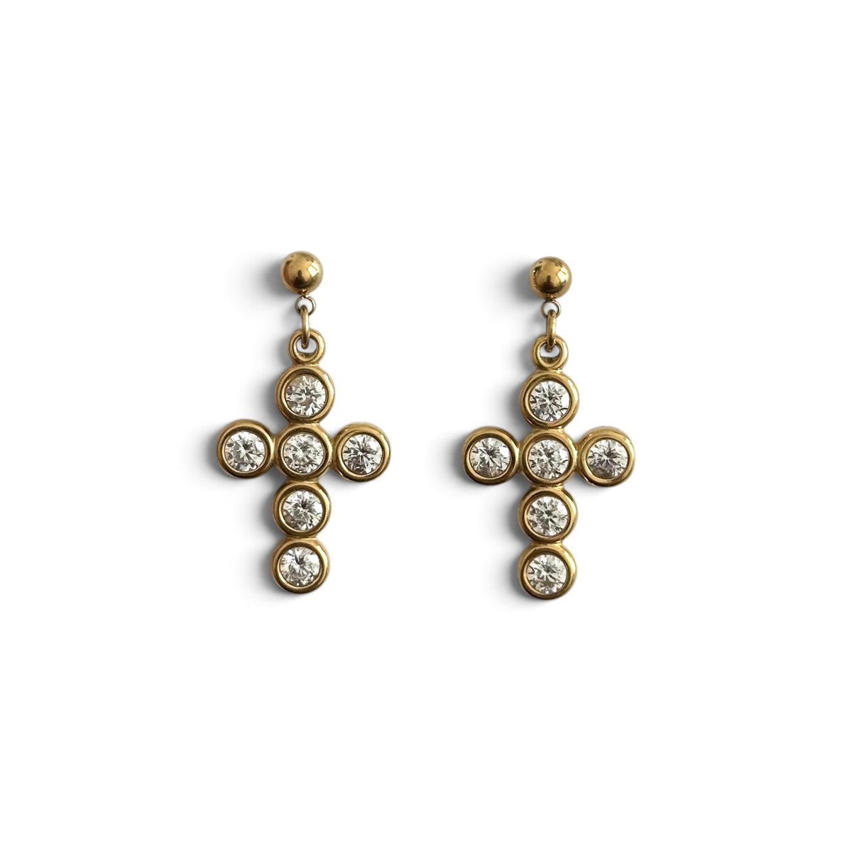 Boucles d’oreilles Livia en acier inoxydable PVD or 18K, pendentifs croix dorés ornés de zircons sur fond blanc.