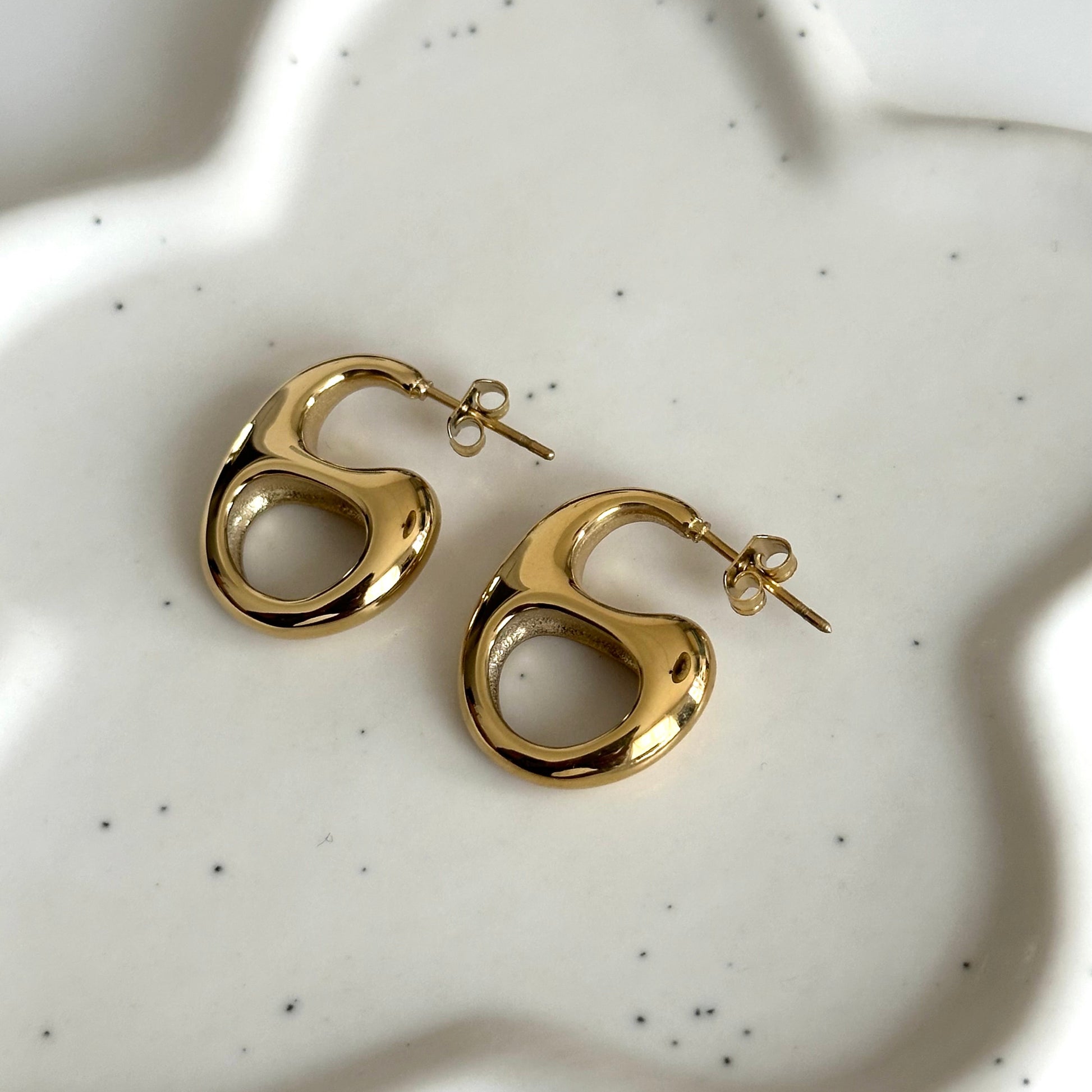 Détail des boucles d’oreilles Thylane dorées à la forme organique et finition brillante.