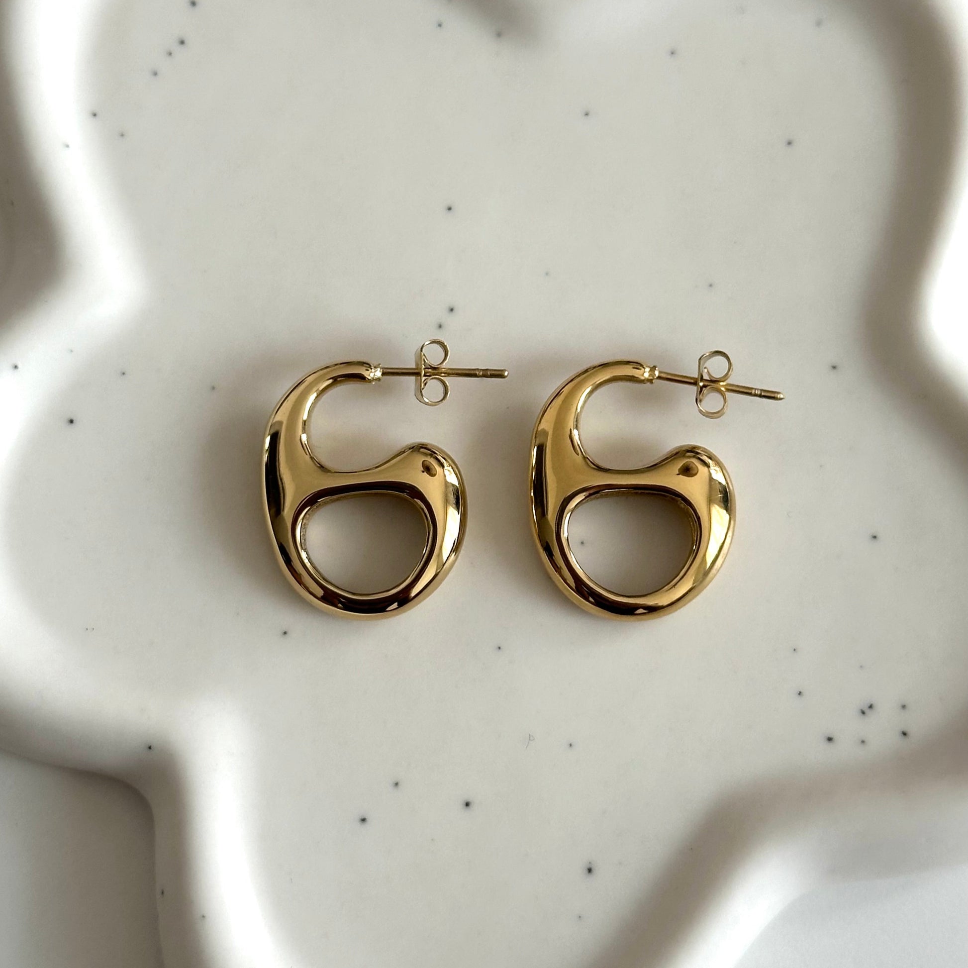Boucles d’oreilles Thylane dorées au design arrondi et ajouré présentées sur fond en céramique blanche.
