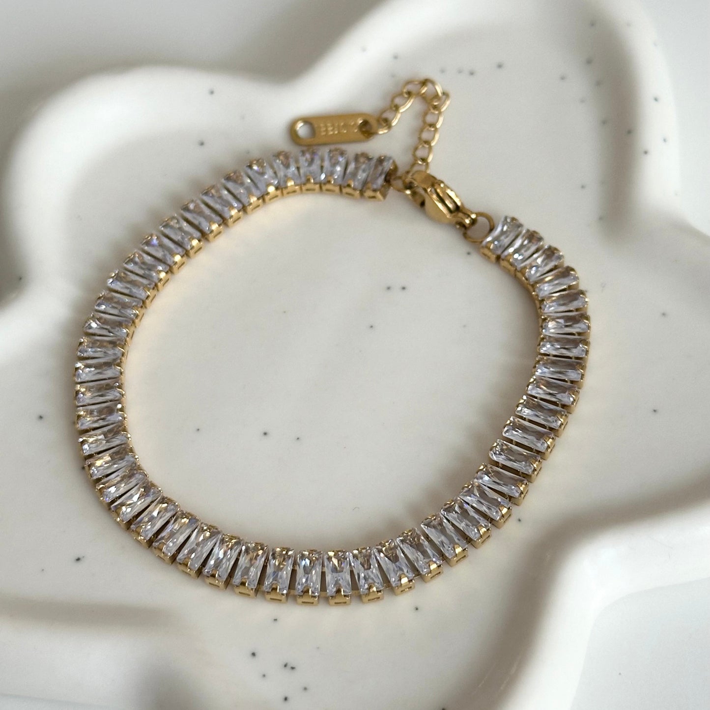 Bracelet tennis Kezia doré avec rangée de zircons rectangulaires et chaîne d’extension.