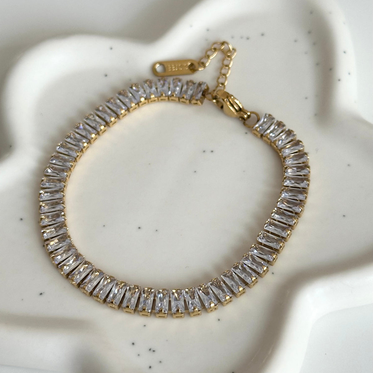Bracelet tennis Kezia doré avec rangée de zircons rectangulaires et chaîne d’extension.