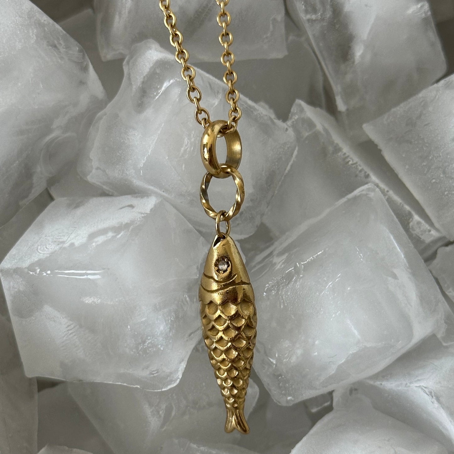Collier Ariel en acier inoxydable doré avec pendentif poisson texturé présenté dans des glaçons.