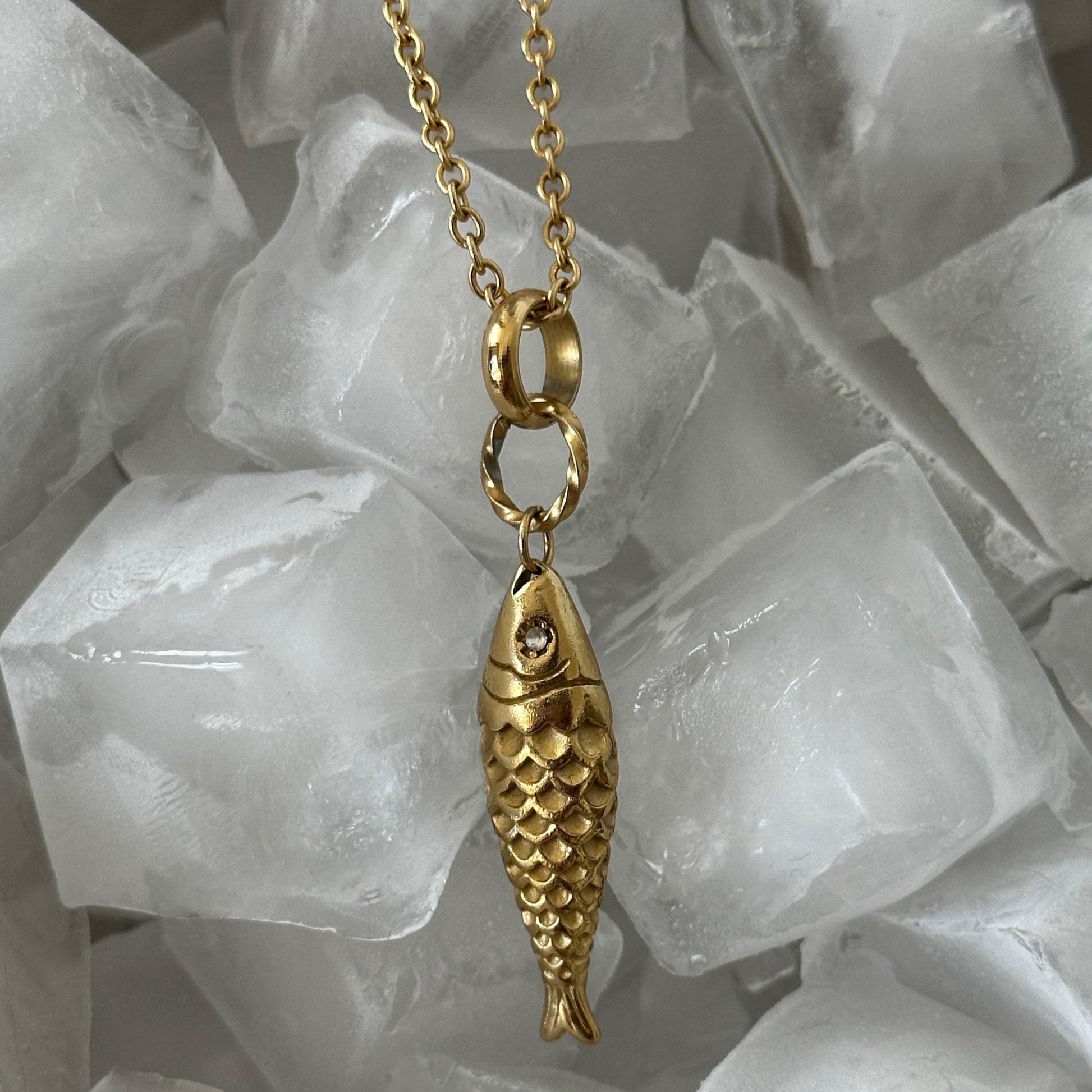 Collier Ariel en acier inoxydable doré avec pendentif poisson texturé présenté dans des glaçons.