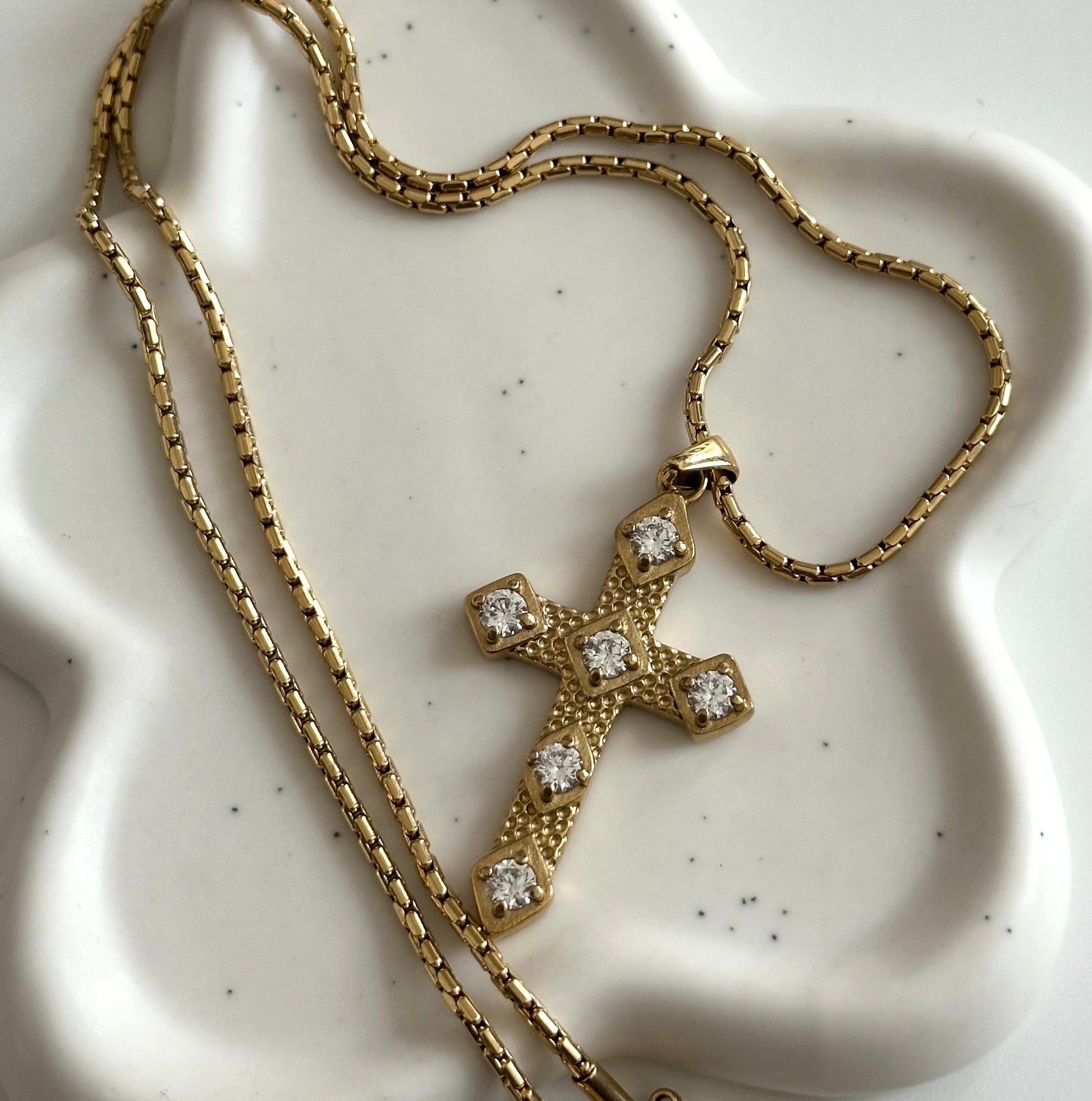 Collier Gina en acier inoxydable PVD or 18K posé sur support blanc avec pendentif croix doré et zircons.