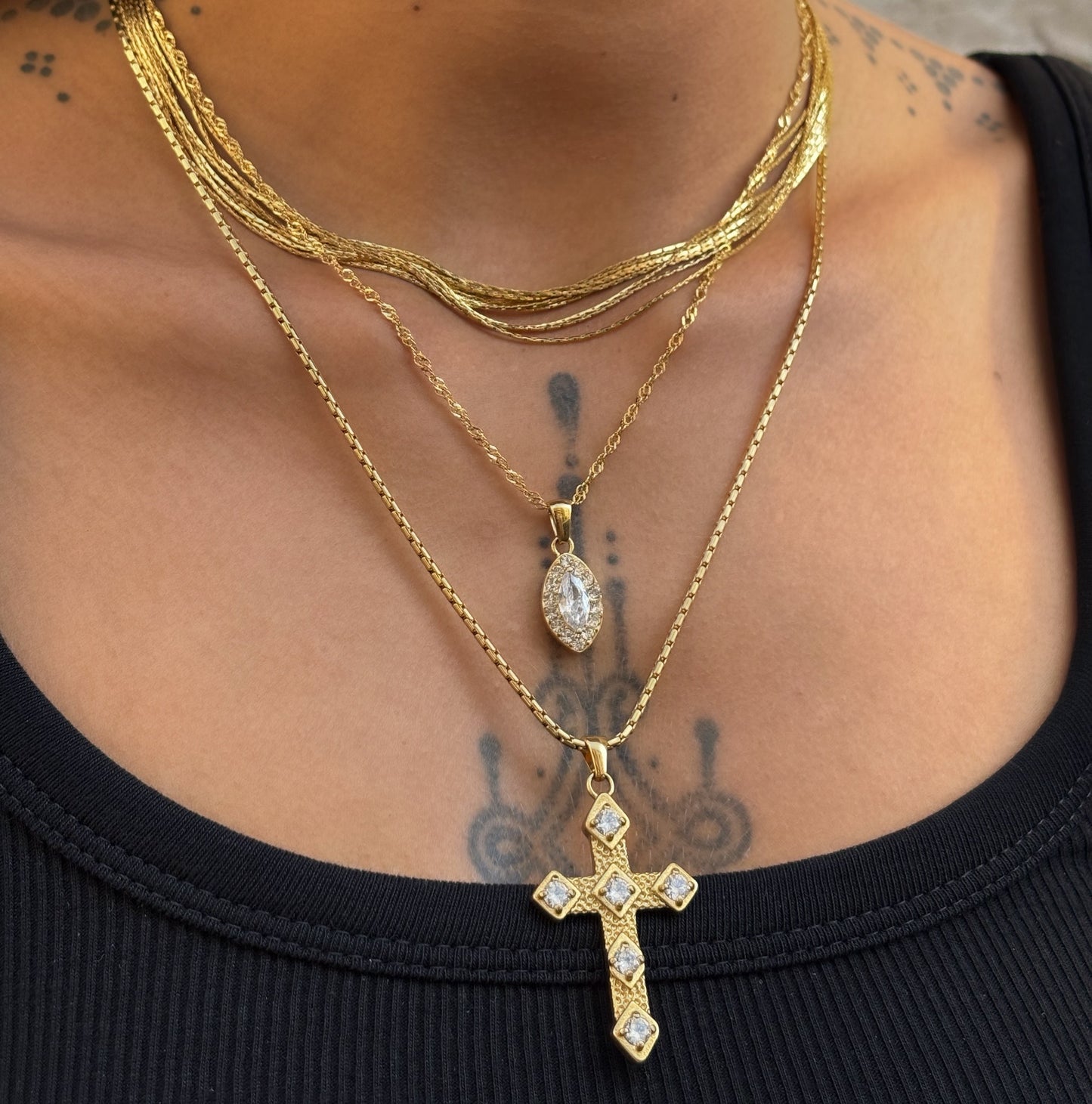 Collier Gina doré en acier inoxydable PVD or 18K porté en accumulation, avec pendentif croix orné de zircons.