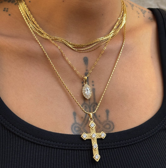Collier Gina doré en acier inoxydable PVD or 18K porté en accumulation, avec pendentif croix orné de zircons.