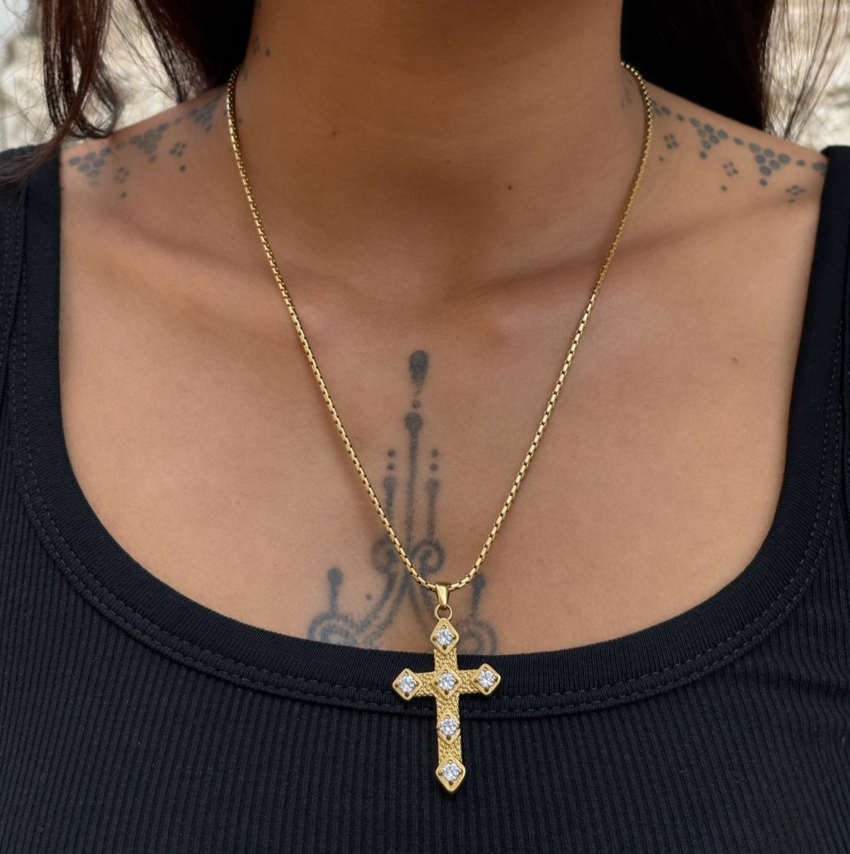 Collier Gina doré en acier inoxydable PVD or 18K porté en accumulation, avec pendentif croix orné de zircons.