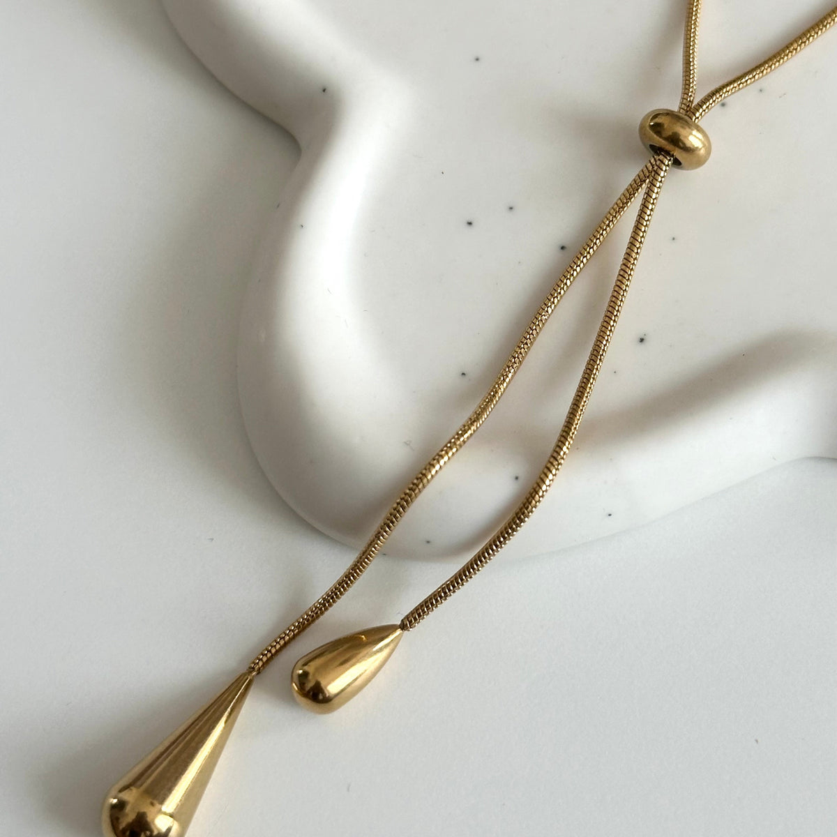 Détail du collier Jane doré avec boule centrale coulissante et pendentifs goutte.