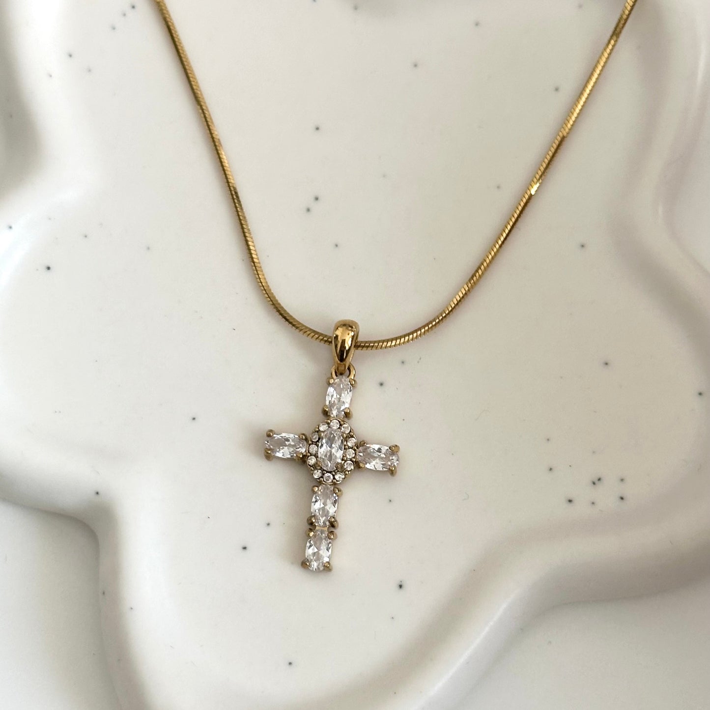 Collier Maria doré en acier inoxydable PVD or 18K avec pendentif croix en zircons présenté sur support blanc.