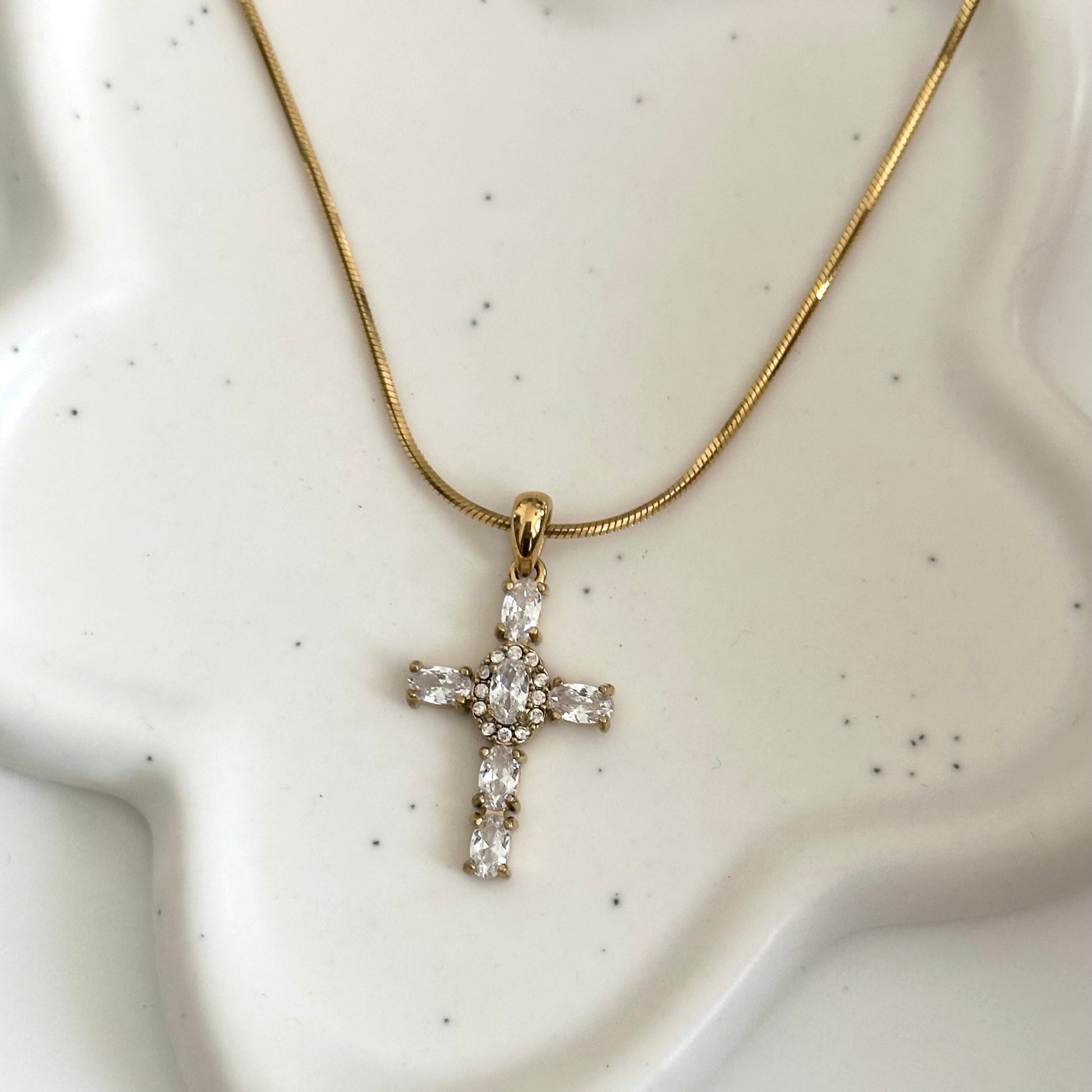 Collier Maria doré en acier inoxydable PVD or 18K avec pendentif croix en zircons présenté sur support blanc.