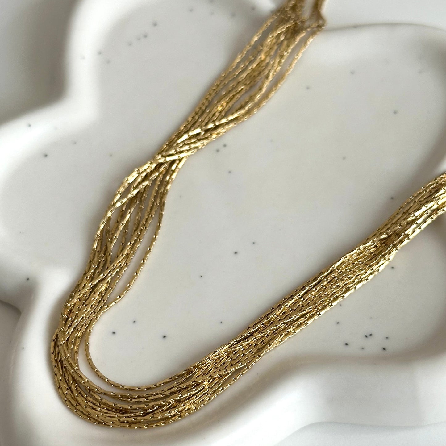 Détail des fines chaînes texturées dorées du collier multirangs Pao.